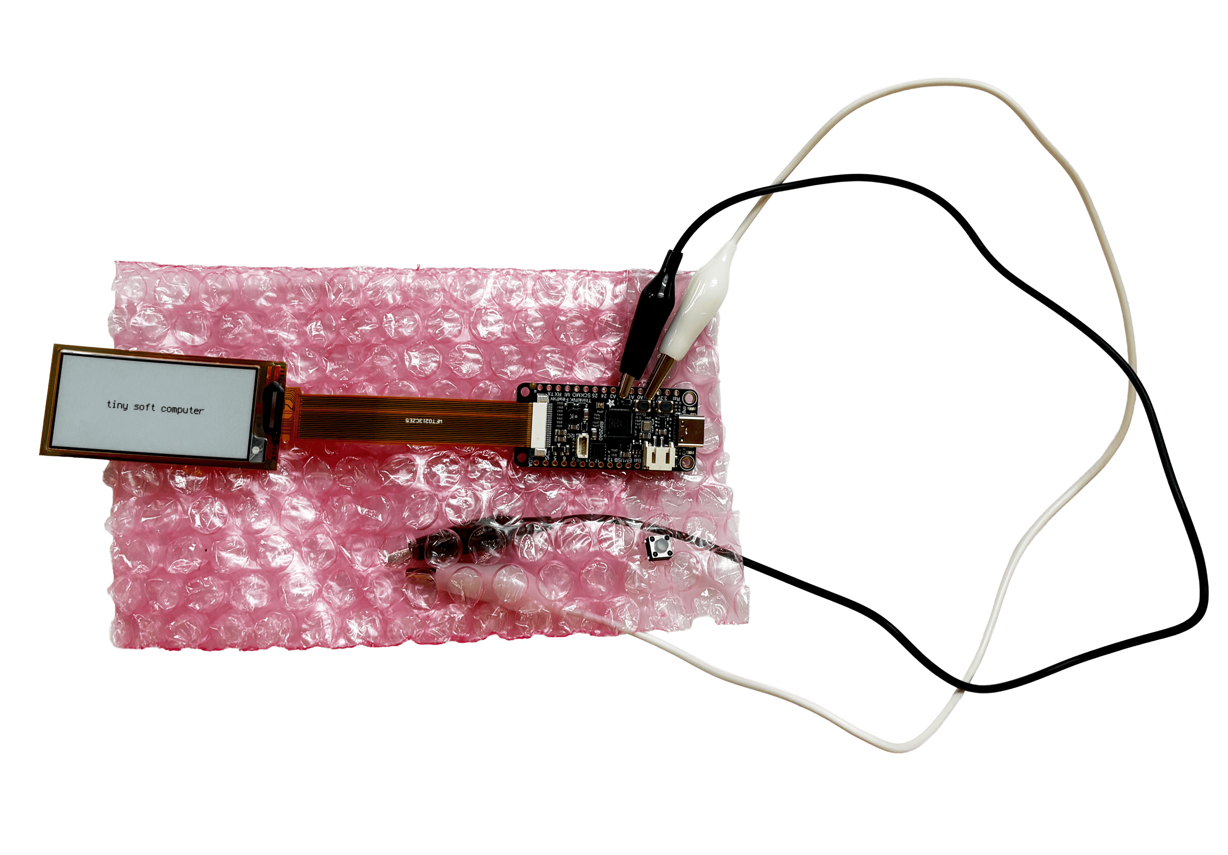 A finished tiny soft computer enclosure, using pink bubble wrap, with the eInk screen and a button on an alligator clip visible through the wrap.