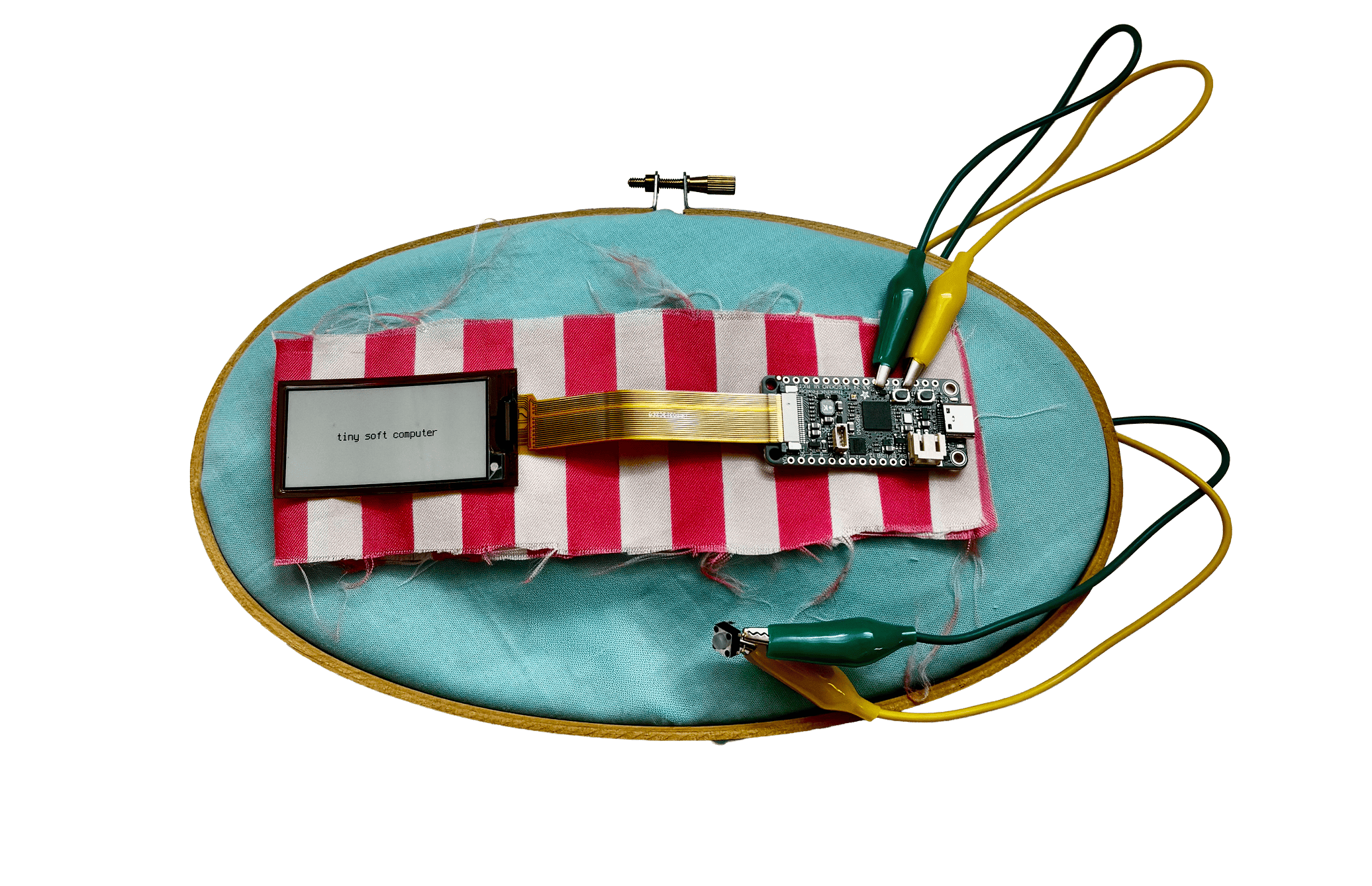 A finished tiny soft computer enclosure, crafted with various soft materials and embroidery hoop, with the eInk screen and a button on an alligator clips.